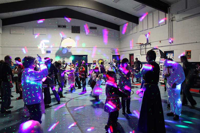 School Light Show, DJ Hamilton, Family dance with guests in costume. Light patterns and dots covering walls. floors & guests. Guests clothes are glowing in the black light beam. Taken in Hamilton Ontario.